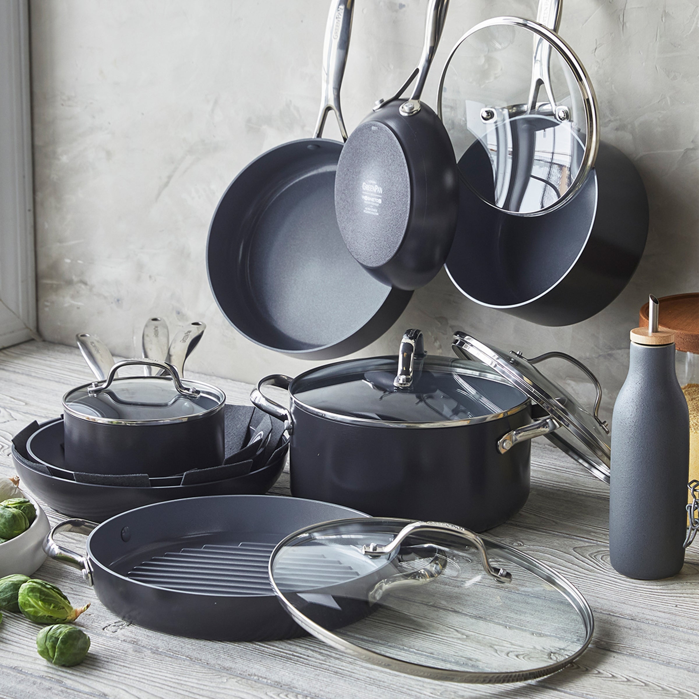 Thirteen-piece ceramic cookware set with glass lids arranged on a light wooden kitchen counter.