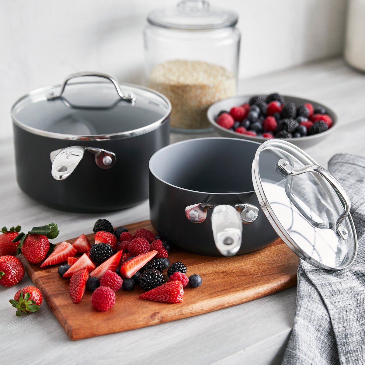 The Valencia Pro Ceramic Nonstick 1.5-Quart and 3-Quart Saucepan Set with Lids in gray sits on a kitchen counter, ready to help you prepare fresh recipes with its scratch-resistant surface—perfect for berries, grains, and everyday cooking.