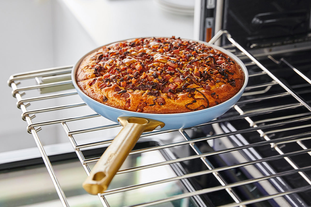 Focaccia bread with herbs and vegetables in a blue GreenPan ceramic pan on an oven rack.