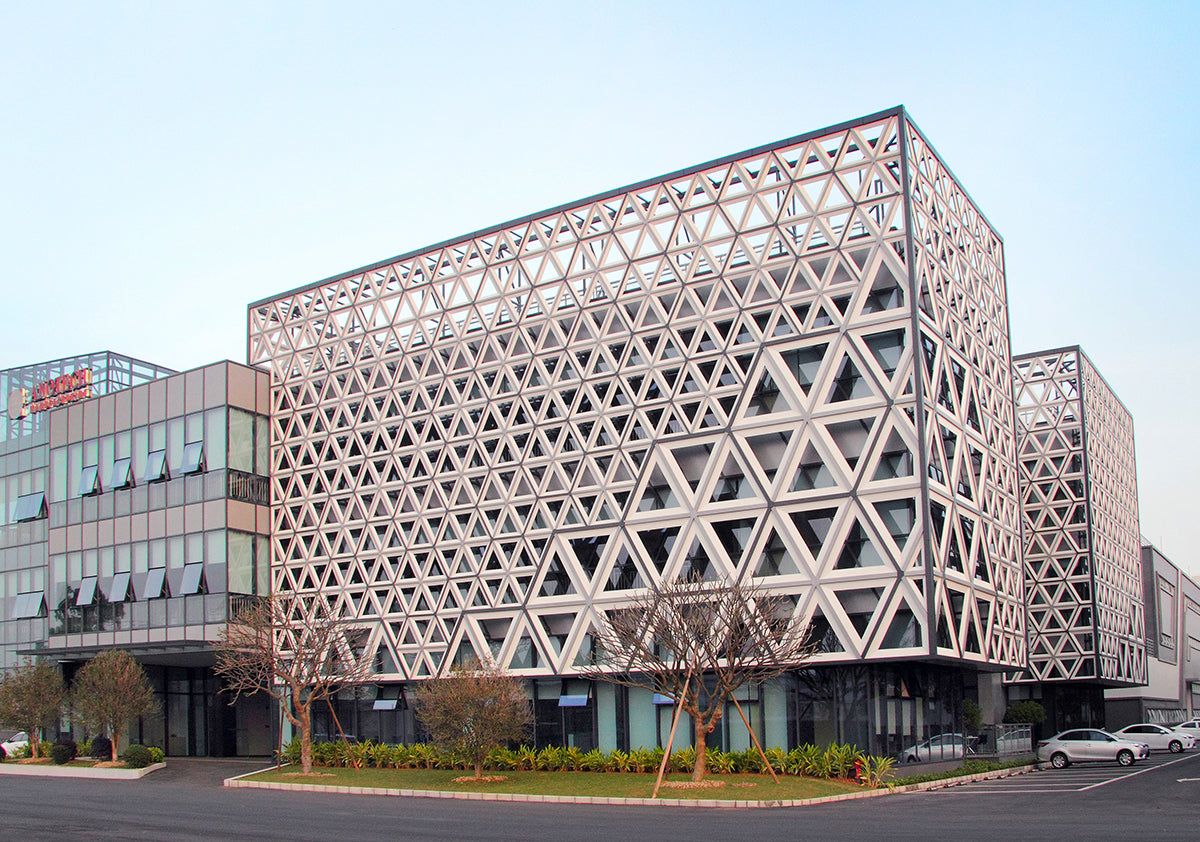 Modern building with a triangular-patterned facade, large windows, and nearby trees and parked cars.