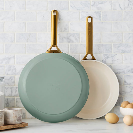 Two green frying pans with gold handles on a kitchen counter.
