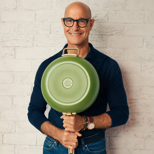 Stanley Tucci holding a green saute pan a light brick wall
