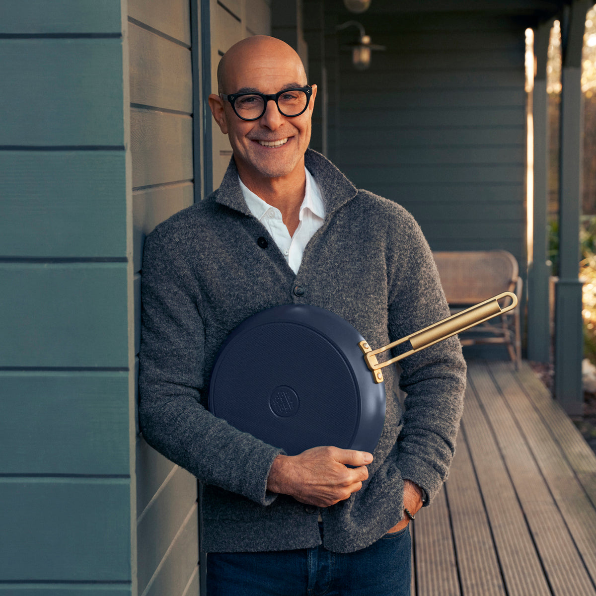 Stanley Tucci holding a blue frying pan on a porch