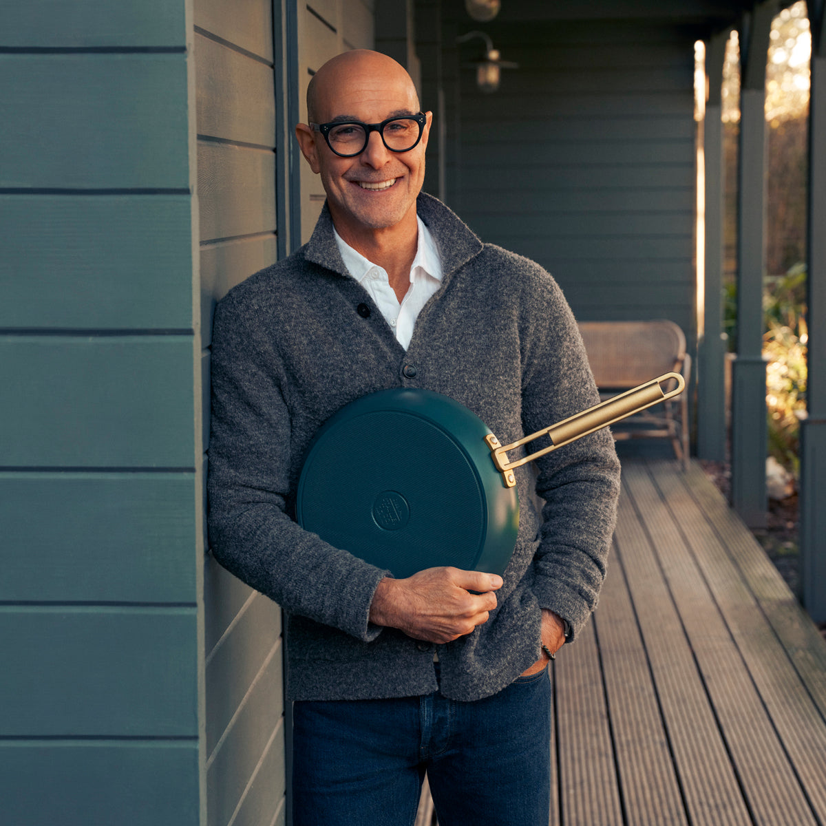 Stanley Tucci holding a teal frypan on a porch